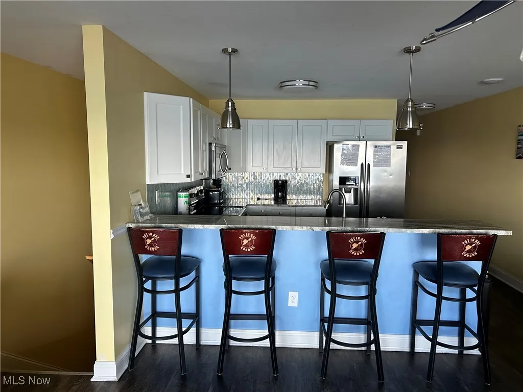 Kitchen with stainless steel appliances, a peninsula, backsplash, and decorative light fixtures