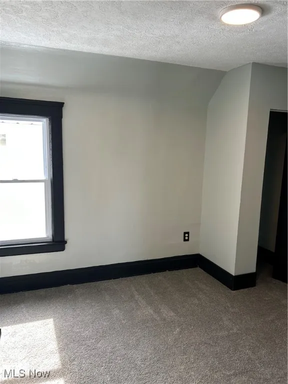 Carpeted empty room with a textured ceiling and baseboards