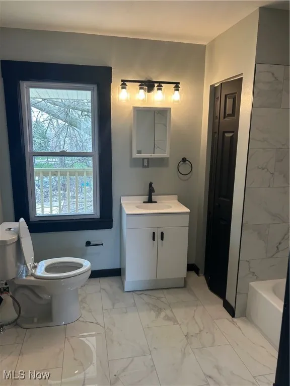 Full bathroom with a bathing tub, toilet, marble finish floor, and baseboards