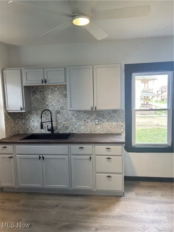Kitchen featuring light wood-type flooring, backsplash, a ceiling fan, dark countertops, and a sink