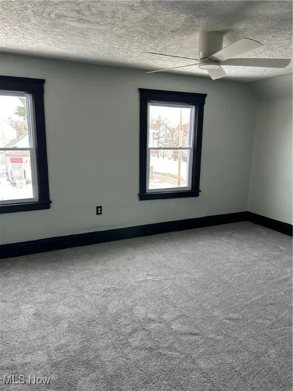 Unfurnished room with a textured ceiling, baseboards, plenty of natural light, and carpet floors