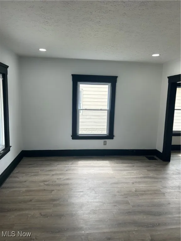 Unfurnished room featuring a textured ceiling, visible vents, recessed lighting, wood finished floors, and baseboards