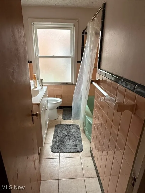 Bathroom with toilet, tile patterned floors, tile walls, and a textured ceiling
