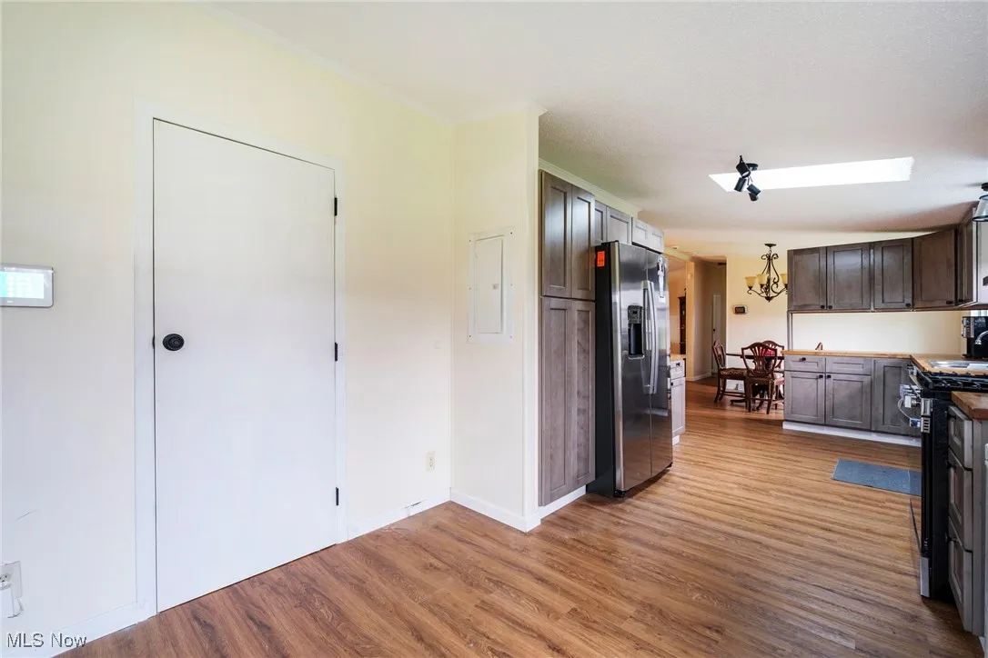 Kitchen with crown molding, electric panel, a chandelier, appliances with stainless steel finishes, and wood finished floors