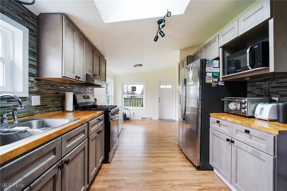 Kitchen featuring under cabinet range hood, a sink, stainless steel gas range oven, butcher block countertops, and light wood finished floors