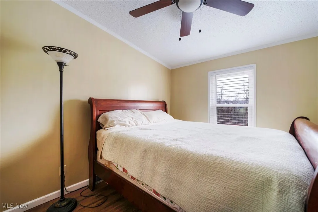 Bedroom featuring ceiling fan, a textured ceiling, ornamental molding, vaulted ceiling, and wood finished floors