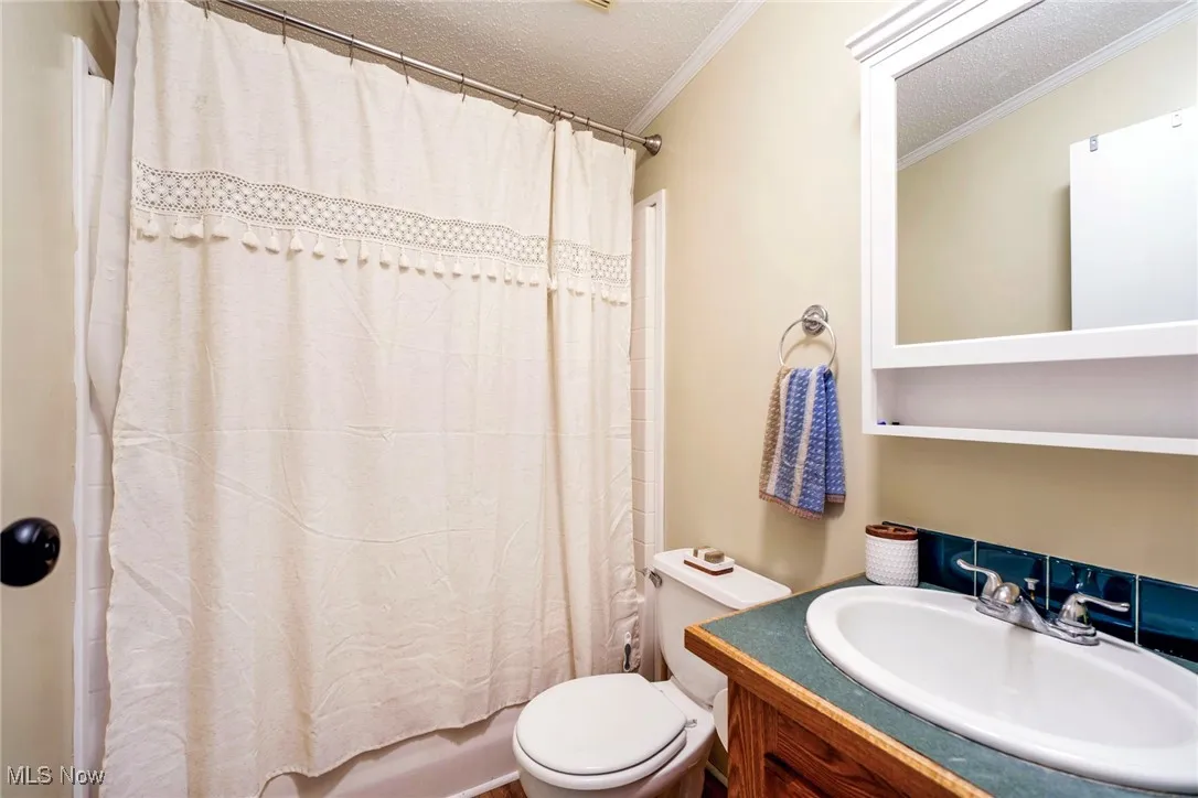 Full bathroom featuring a textured ceiling, shower / bathtub combination with curtain, vanity, ornamental molding, and toilet