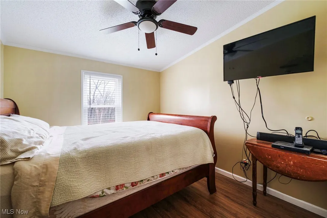 Bedroom featuring crown molding, ceiling fan, a textured ceiling, wood finished floors, and baseboards