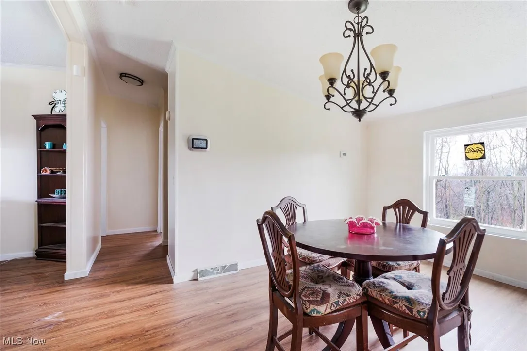 Dining room with baseboards, visible vents, light wood-type flooring, and an inviting chandelier