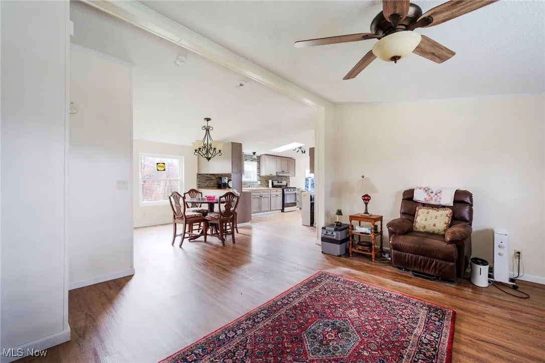 Sitting room with light wood-style floors, ceiling fan with notable chandelier, and baseboards