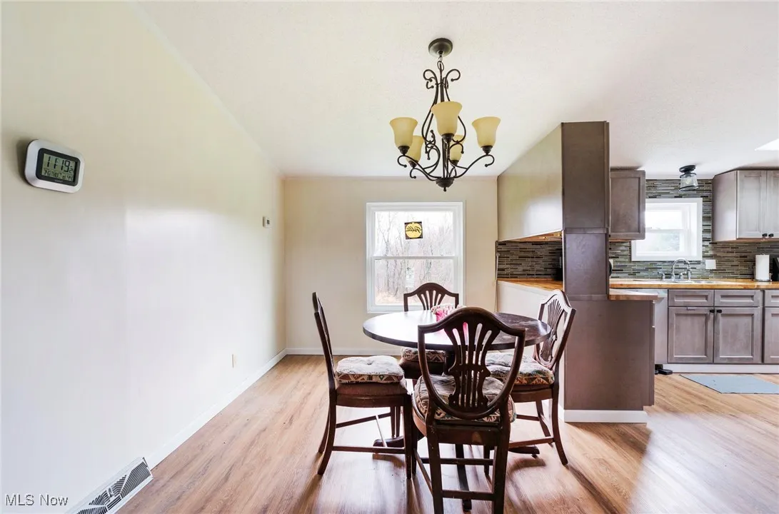 Dining area with a wealth of natural light, visible vents, light wood-type flooring, and an inviting chandelier