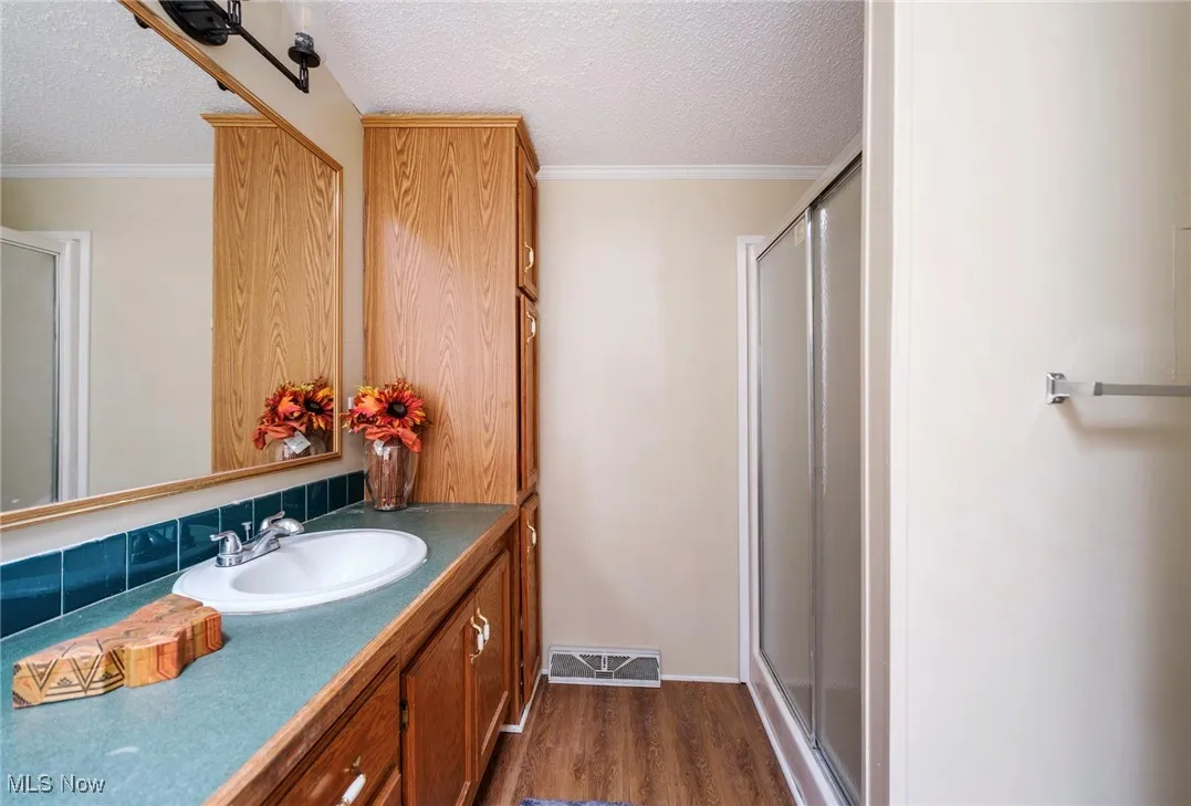 Full bathroom featuring vanity, a textured ceiling, a shower stall, visible vents, and wood finished floors