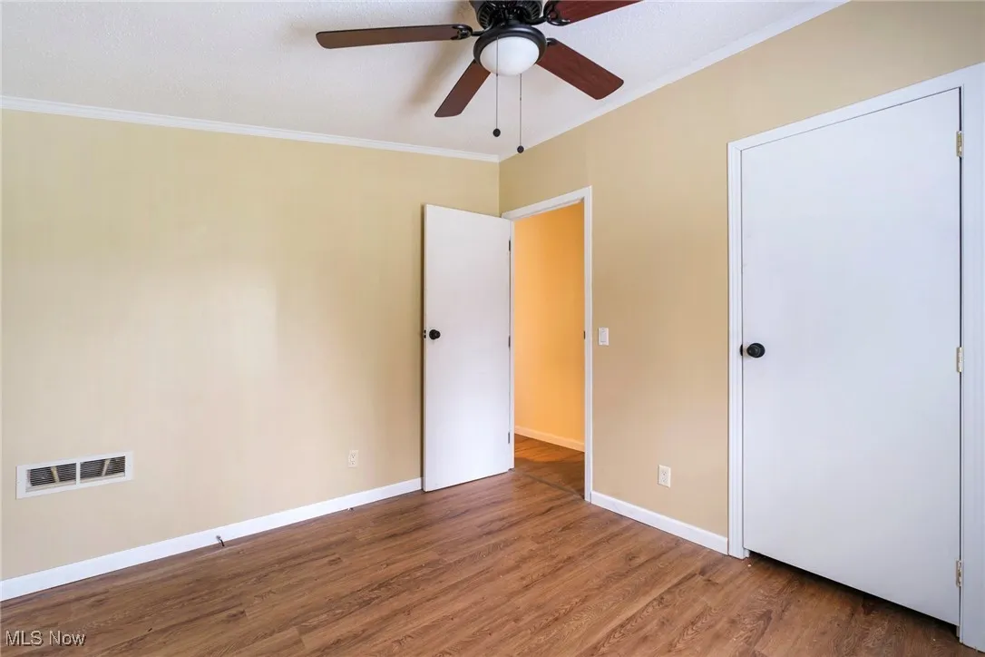 Unfurnished bedroom with visible vents, baseboards, ornamental molding, ceiling fan, and wood finished floors