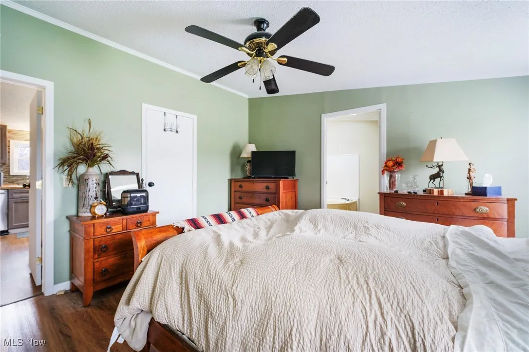 Bedroom featuring ornamental molding, ceiling fan, ensuite bath, and wood finished floors