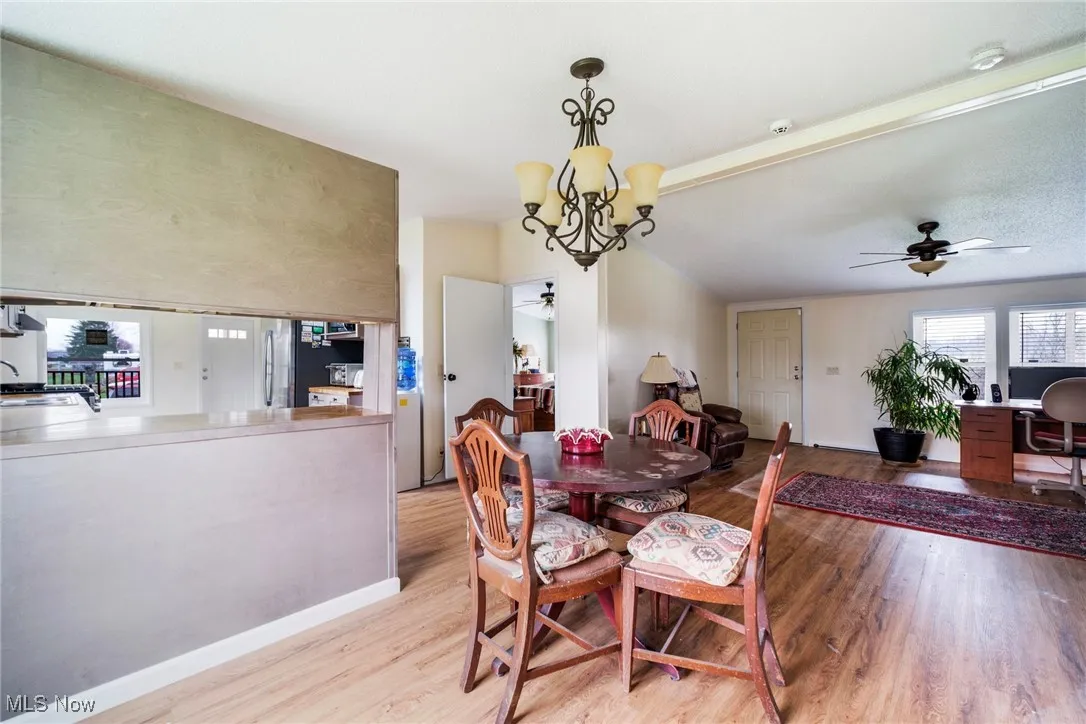 Dining space with light wood-type flooring, ceiling fan with notable chandelier, and baseboards