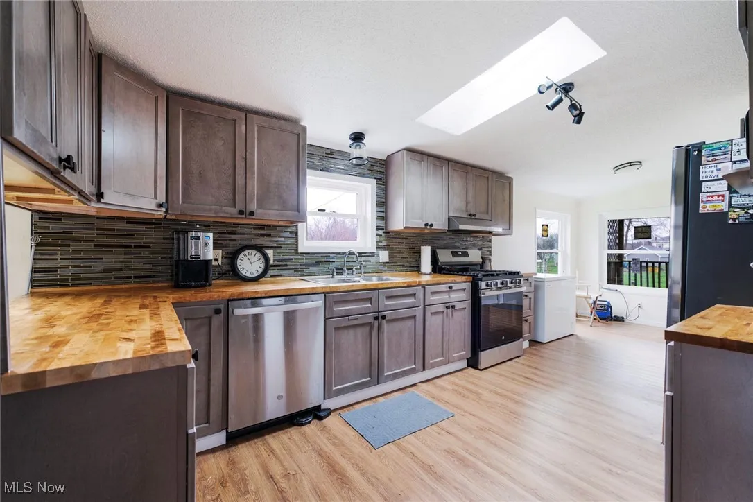 Kitchen with a sink, light wood-type flooring, butcher block counters, stainless steel appliances, and decorative backsplash