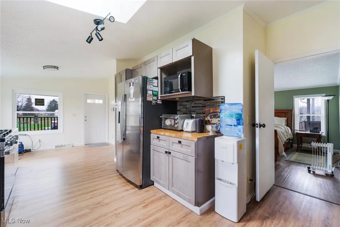 Kitchen with visible vents, stainless steel fridge, wooden counters, light wood-type flooring, and black microwave