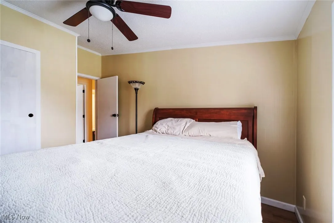 Bedroom with ornamental molding, ceiling fan, wood finished floors, and baseboards