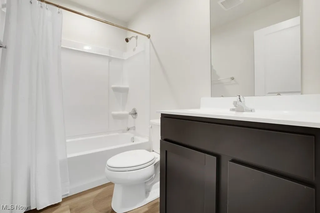 Full bathroom with vanity, visible vents, toilet, shower / bath combo, and wood finished floors