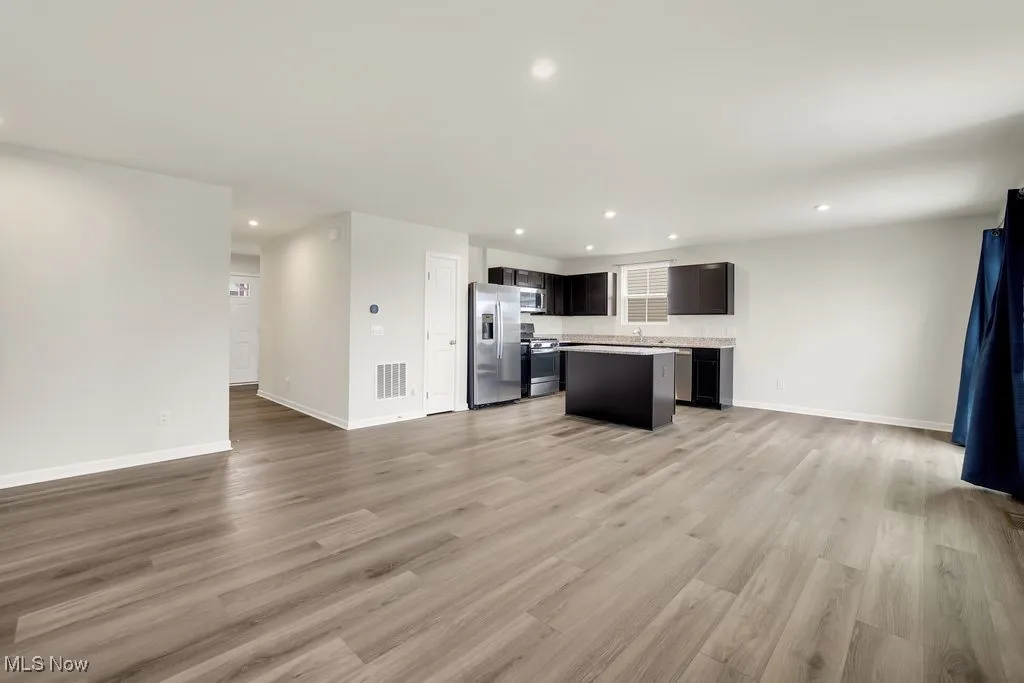 Kitchen with open floor plan, a kitchen island, visible vents, light wood-style floors, and stainless steel appliances
