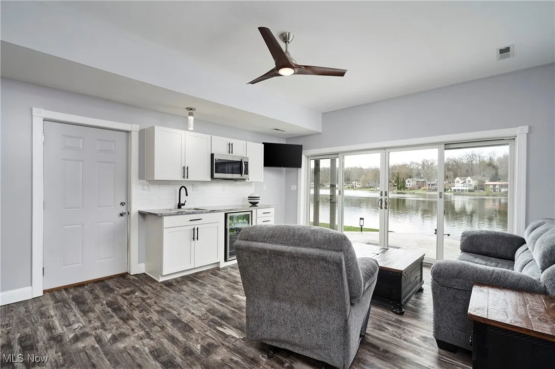 Living room with indoor wet bar, dark wood-type flooring, visible vents, a water view, and beverage cooler