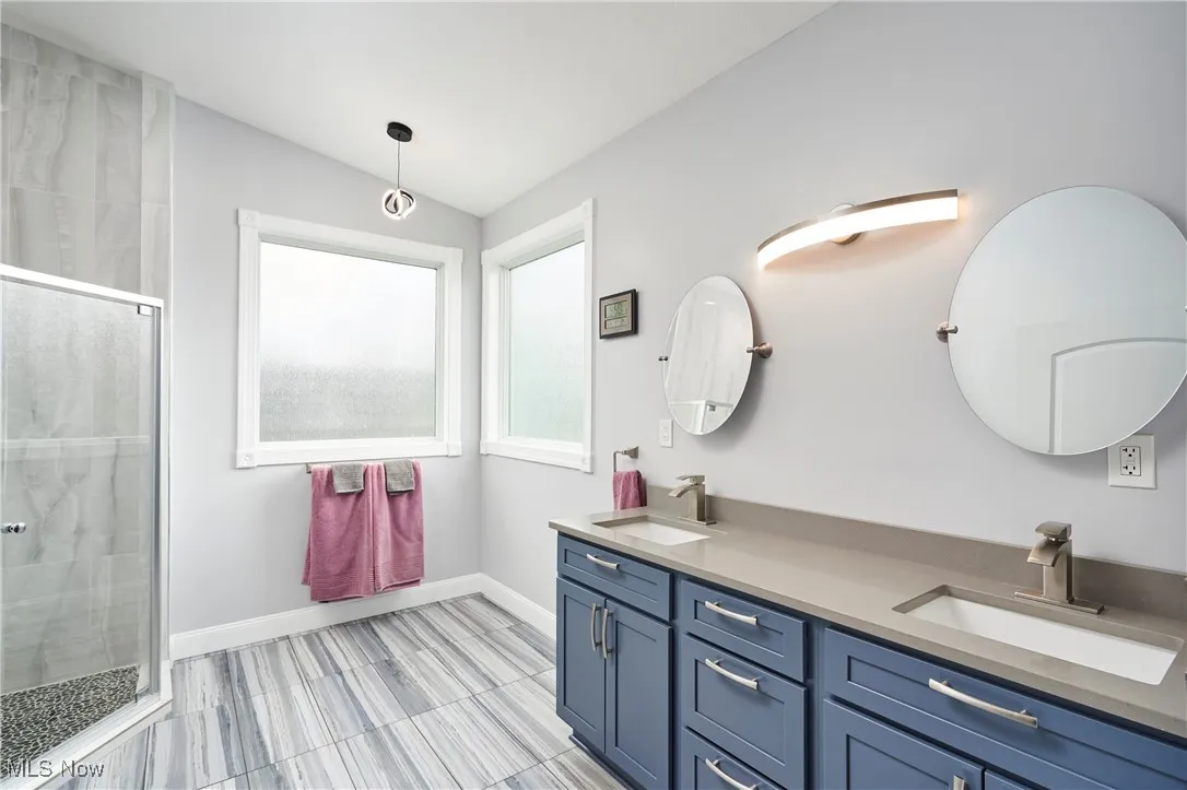 Full bathroom featuring a sink, a tile shower, double vanity, and baseboards