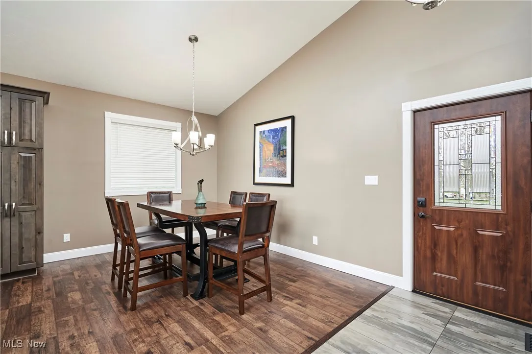 Dining room featuring wood finished floors, high vaulted ceiling, a notable chandelier, and baseboards