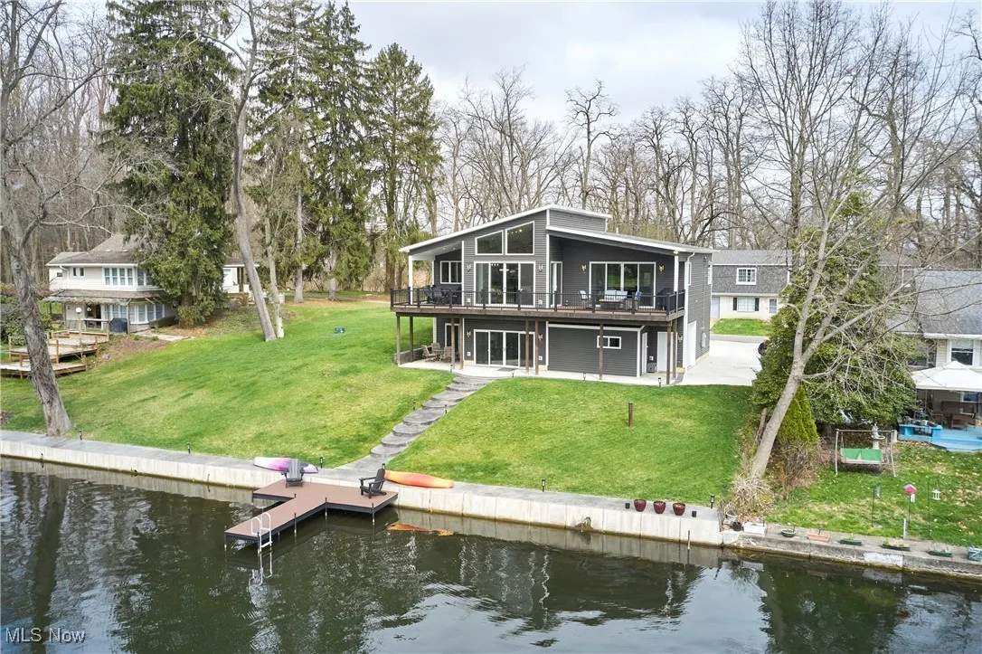 Back of house with a patio area, a deck with water view, and a lawn