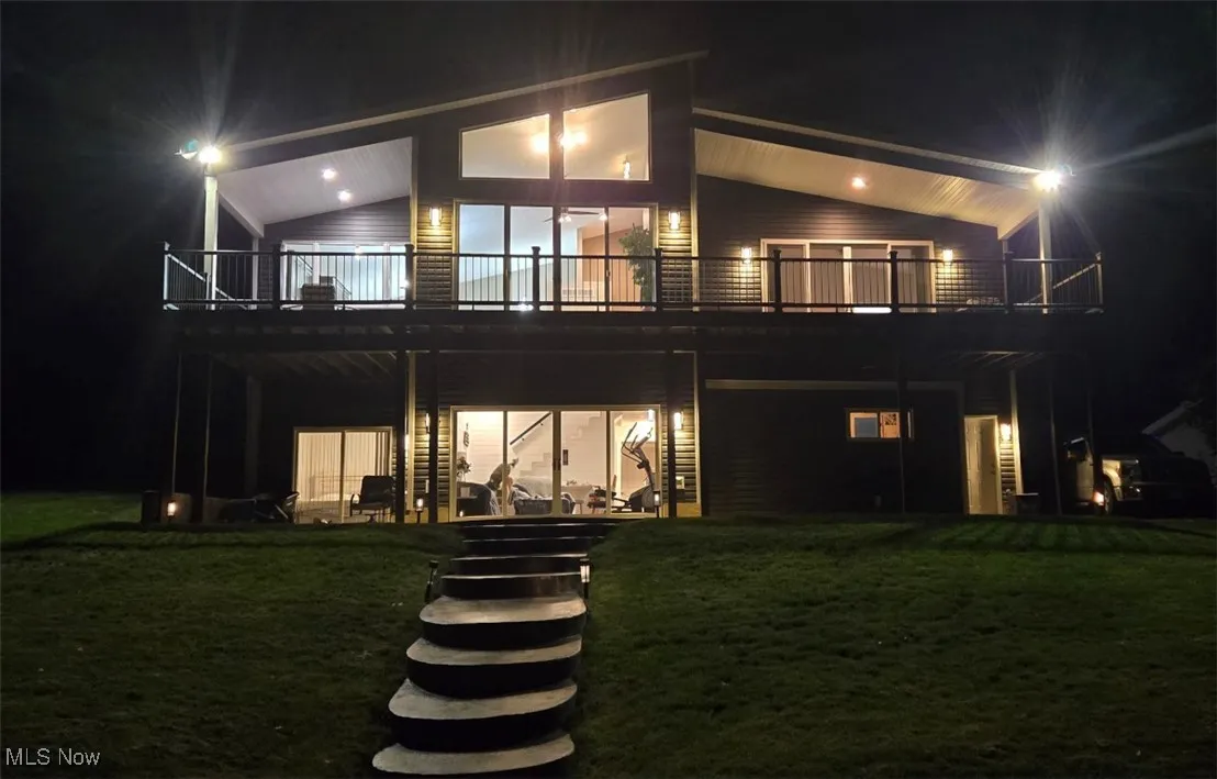 Back of house at twilight with a deck, a lawn, and stairs