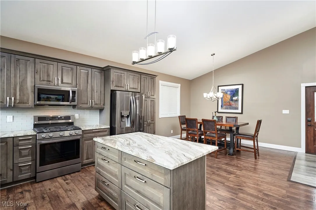Kitchen featuring a notable chandelier, vaulted ceiling, dark wood-style floors, backsplash, and appliances with stainless steel finishes