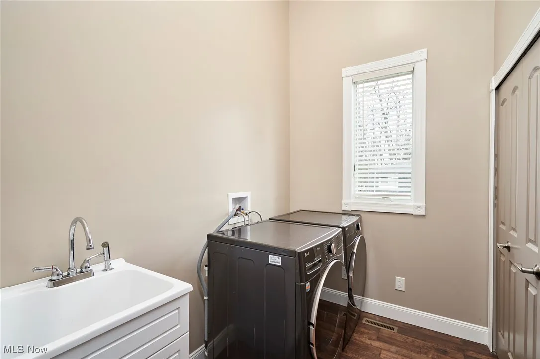 Main level washroom featuring baseboards, a sink, laundry area, dark wood-type flooring, and washer and clothes dryer