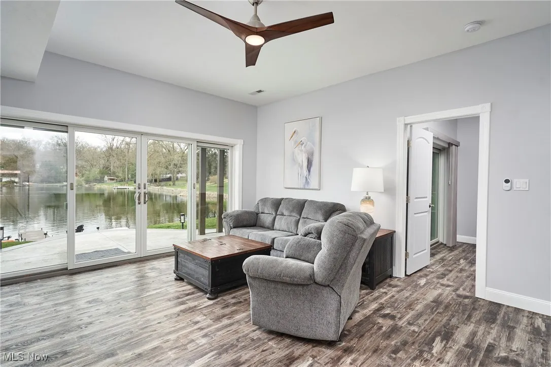 Living area with a ceiling fan, visible vents, a water view, wood finished floors, and baseboards