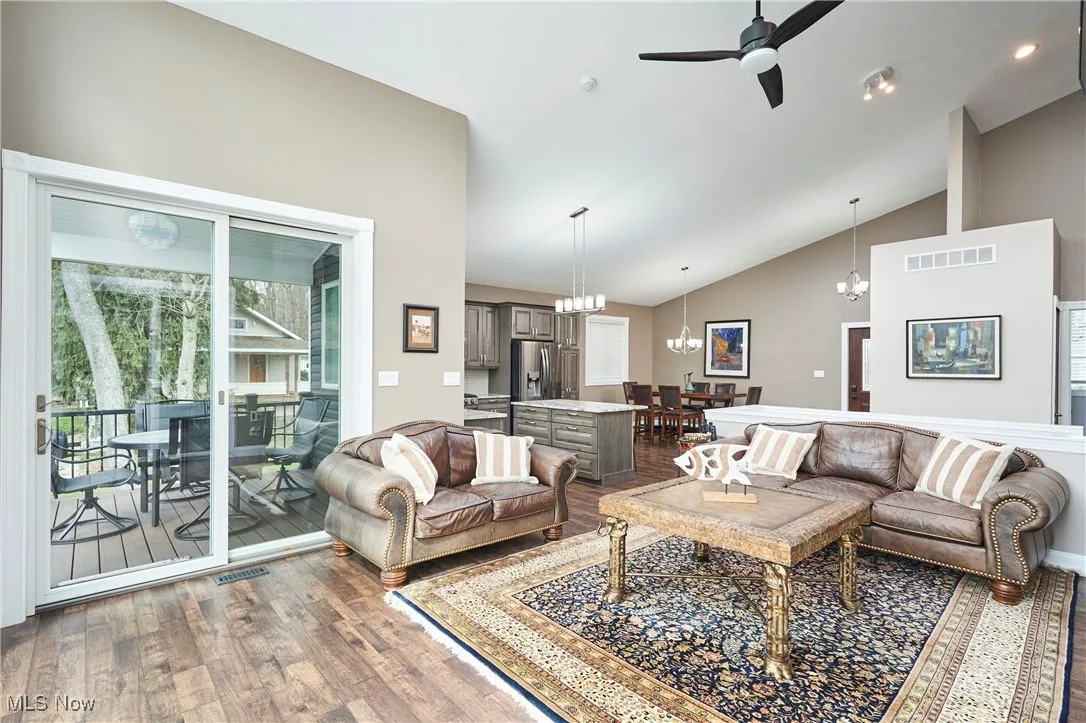 Living room featuring wood finished floors, ceiling fan with notable chandelier, visible vents, and high vaulted ceiling