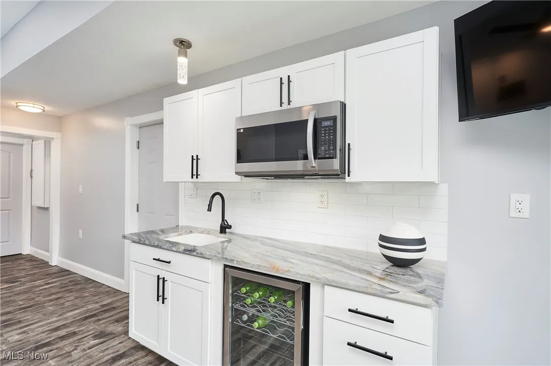 Kitchen featuring baseboards, a sink, wine cooler, stainless steel microwave, and decorative backsplash