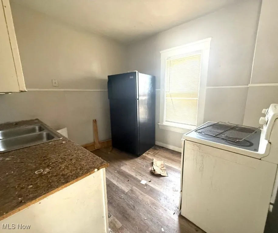 Kitchen with a sink, dark countertops, freestanding refrigerator, wood finished floors, and washer / dryer