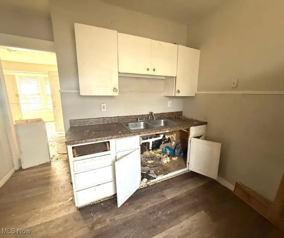 Kitchen featuring white cabinets, dark wood finished floors, a sink, and dark countertops