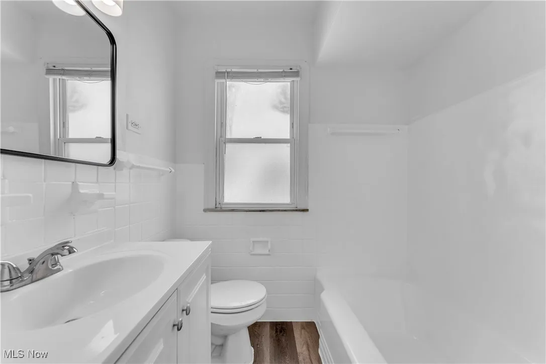Bathroom with tile walls, wood finished floors, a tub, vanity, and wainscoting