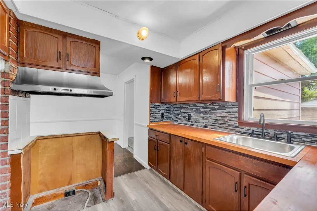 Kitchen featuring decorative backsplash, under cabinet range hood, light wood-style flooring, brown cabinets, and plenty of natural light