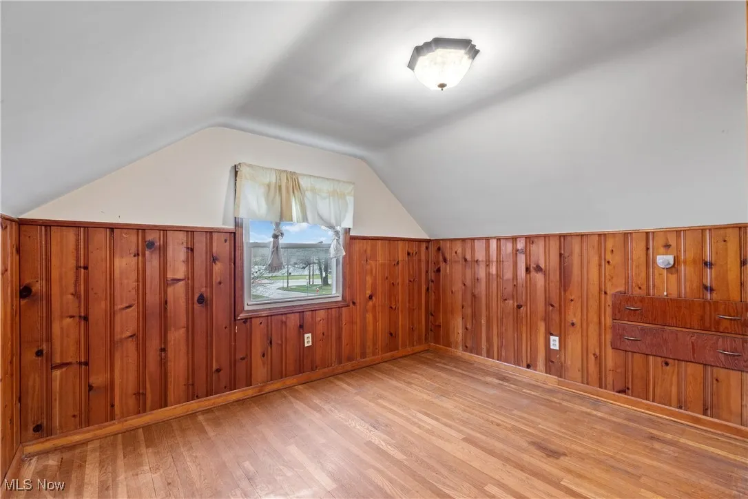 Additional living space with wood finished floors, wooden walls, lofted ceiling, and a wainscoted wall