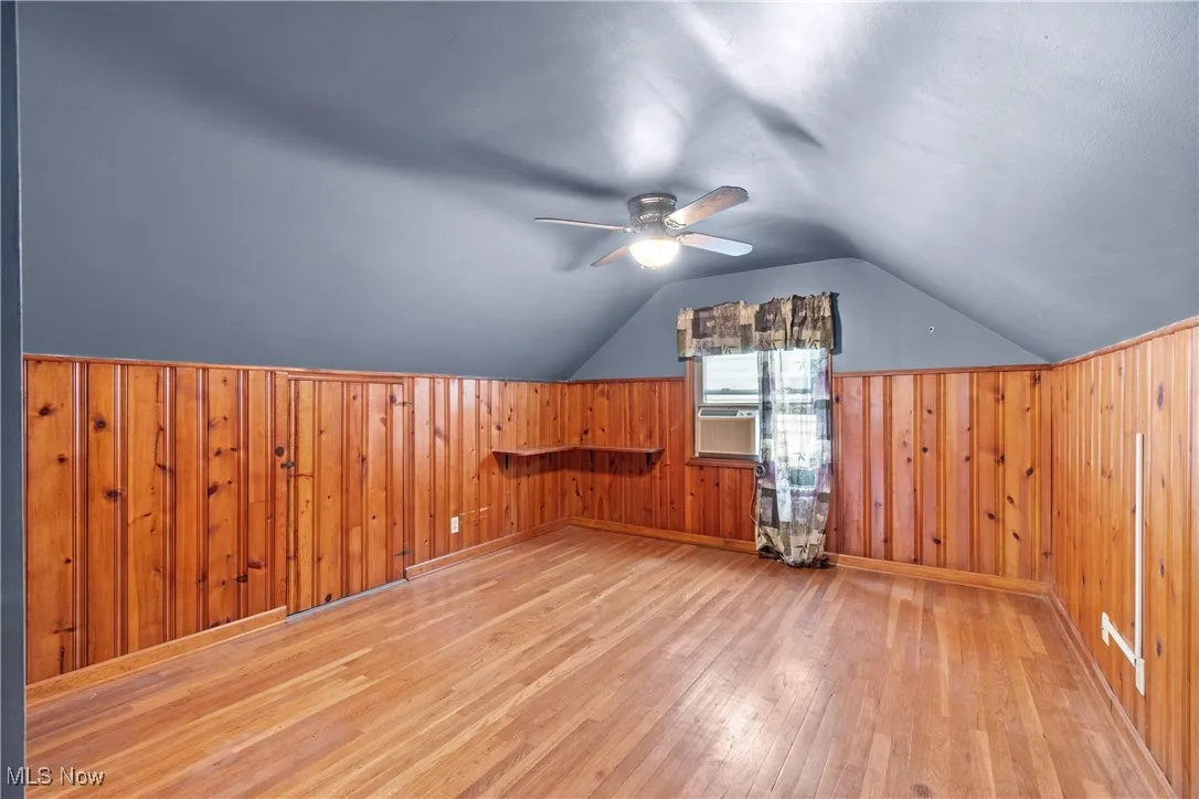 Additional living space featuring hardwood / wood-style floors, wooden walls, a ceiling fan, and vaulted ceiling