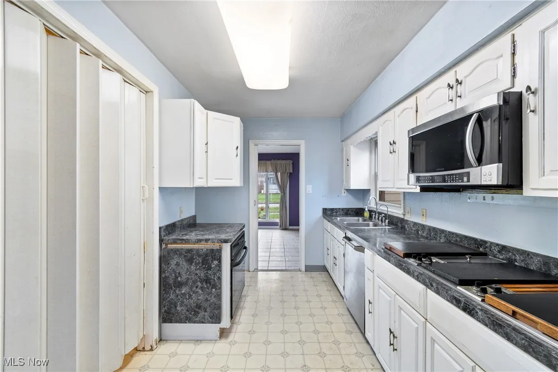 Kitchen with dark countertops, appliances with stainless steel finishes, a sink, and light floors