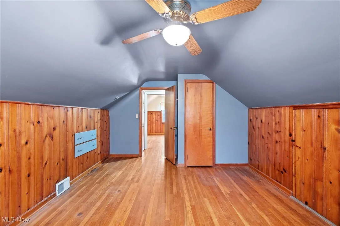 Bonus room featuring wooden walls, visible vents, and hardwood / wood-style flooring