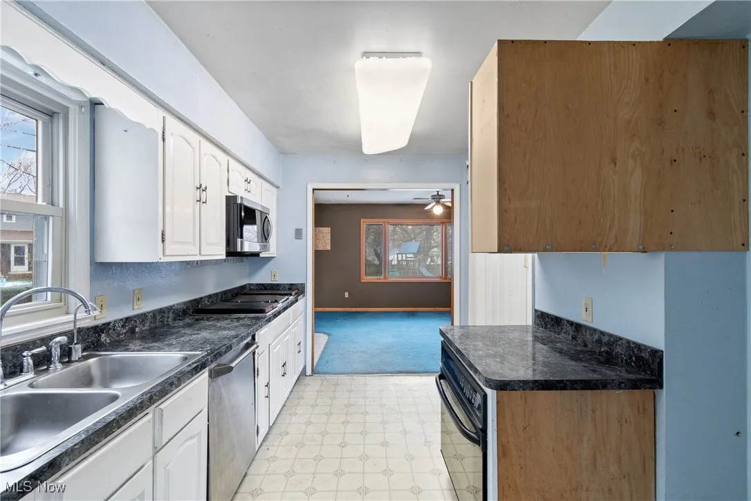 Kitchen with appliances with stainless steel finishes, a sink, white cabinetry, and light floors
