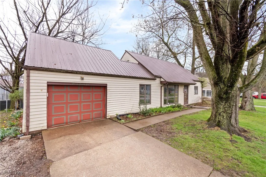 View of front facade with an attached garage, a front lawn, driveway, and metal roof