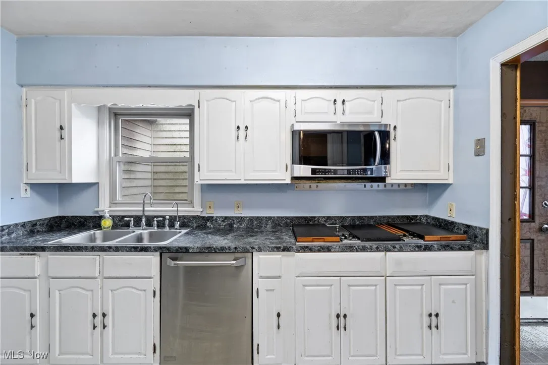 Kitchen with a sink, stainless steel microwave, dark countertops, and white cabinets