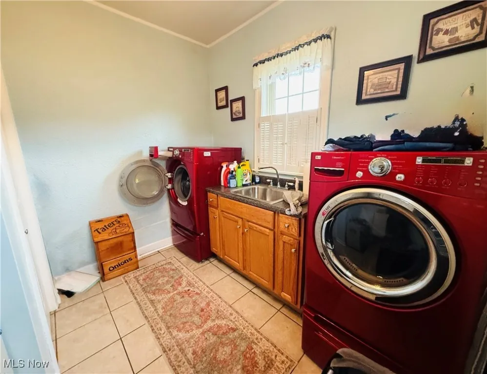 Clothes washing area featuring a sink, crown molding, cabinet space, washing machine and clothes dryer, and light tile patterned flooring