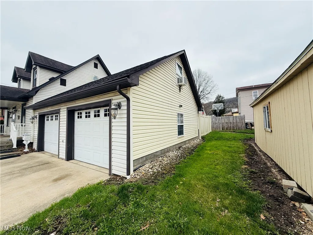 View of property exterior with a yard, fence, and concrete driveway