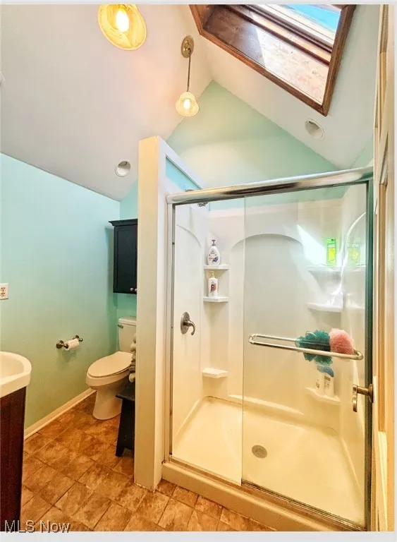 Full bathroom with a shower stall, vanity, lofted ceiling with skylight, toilet, and baseboards