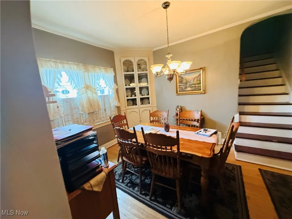 Dining space featuring crown molding, light wood-type flooring, an inviting chandelier, and stairs