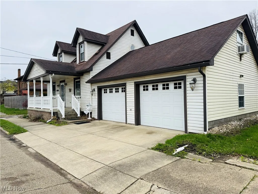 New england style home with a porch, an attached garage, cooling unit, driveway, and roof with shingles